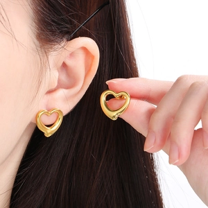 Close-up of golden hollow heart earrings shown on a model and held in hand