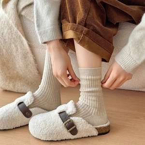 Detail of cream plush mule slippers with brown leather strap and ribbed mid-calf socks