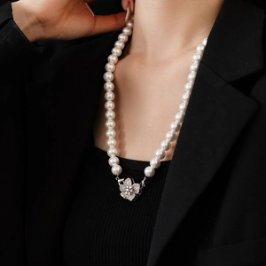 Detail of flower zircon buckle on white faux pearl necklace worn with black suit