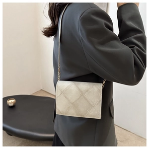 Quilted beige shoulder bag with chain strap shown on a model wearing a dark blazer