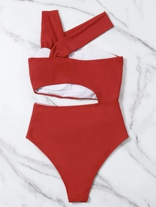 Flat lay of a red one-shoulder monokini featuring stylish waist cut-outs on marble background