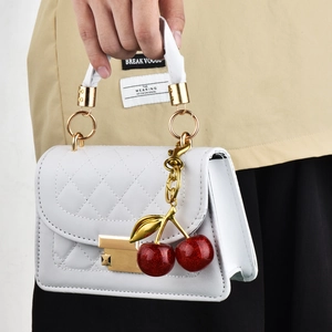 White quilted mini handbag with red cherry charm and gold buckle shown on model