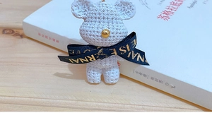 Detail of a white resin bear keychain with a woven texture and golden nose accent