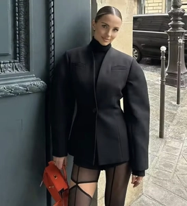 Outdoor street style shot of a woman in a black V-neck puff sleeve blazer and orange handbag