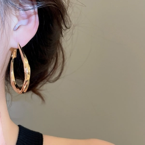 Close-up of elegant gold twisted hoop earring worn by a model in a minimalist style