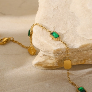 Pulsera de cadena de oro con piedras verdes cuadradas sobre fondo de piedra natural