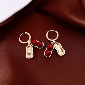 Macro shot of gold-plated peanut earrings with red beads on luxury satin background