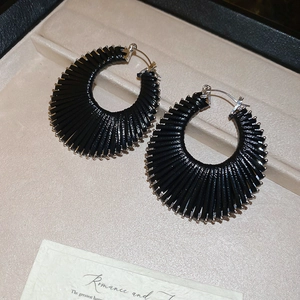 Détail de boucles d'oreilles créoles noires texturées sur un plateau à bijoux en velours