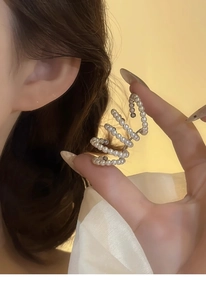Detail of French vintage multilayer pearl ear cuff with elegant spiral design held by a hand