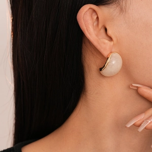 Close-up of elegant gold metal earrings with creamy resin inlay on model's ear