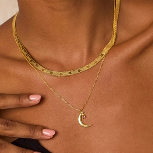 Detail of layered gold moon and star necklace set with a purple zircon on skin