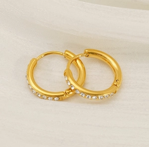 Detail-Makroaufnahme goldener Creolen mit feinem weißen Zirkonbesatz auf Stoffgewebe