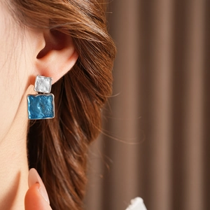 Detail of blue and silver square earrings featuring a unique hammered metal texture