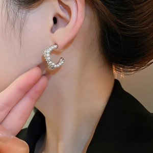 Detail of C-shaped pearl earring with silver metal base and crystals on ear