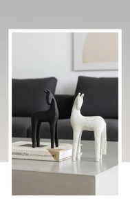 Detail of minimalist horse statues in black and textured white on a gray coffee table