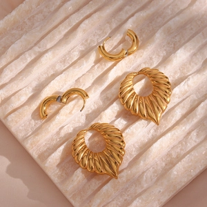 Detail showing gold leaf-shaped earrings and small hoops on a stone background