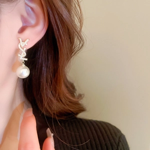 Détail de boucles d'oreilles perles avec monogramme en cristal et placage or sur modèle