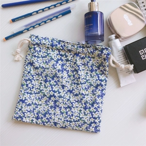 Detailed flat lay of a blue floral cotton drawstring storage bag with cosmetic accessories
