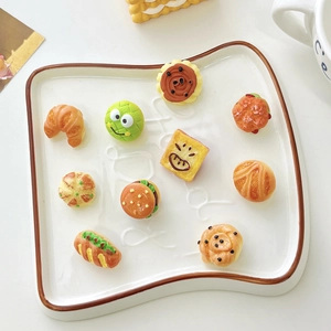 Close-up of cute resin hamburger and croissant badges on a toast-shaped ceramic plate