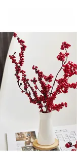 Artificial red berry stems in a white ceramic vase on a wooden mat for Christmas decor