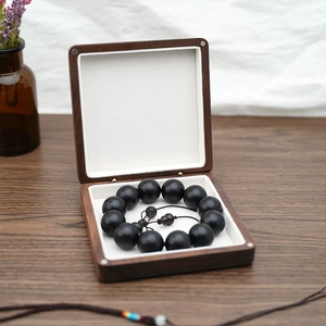 Detail of wooden jewelry box with white velvet lining and black beaded bracelet inside