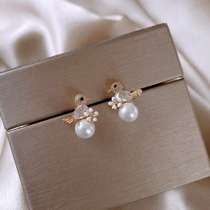Macro shot of bird-shaped gold earrings with diamonds, white enamel flower and hanging pearl