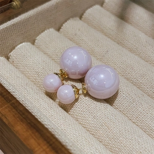 Close-up of lavender pearl stud earrings with gold metal accents in a beige jewelry box