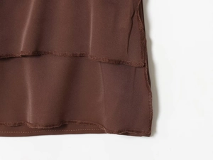 Detail of ruffle hem on brown satin top showing precise stitching and smooth silk-like texture