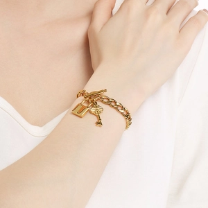 Gros plan d'un bracelet gourmette doré avec pendentifs cadenas et clé sur un mannequin