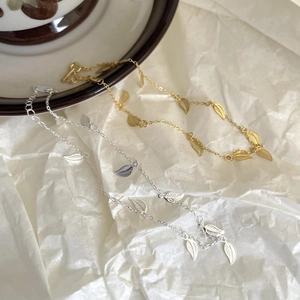 Detail view of 925 sterling silver leaf anklets in gold and silver finishes on white paper