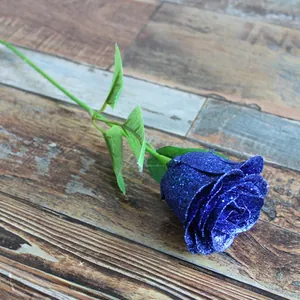 Close-up of artificial blue glitter rose with green leaves on vintage wood floor