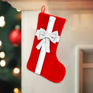 Red plush Christmas stocking with white bow hanging on a mantel with tree lights