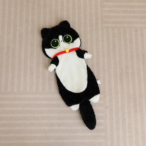 Long coussin chat en peluche noir et blanc avec yeux verts et collier rouge