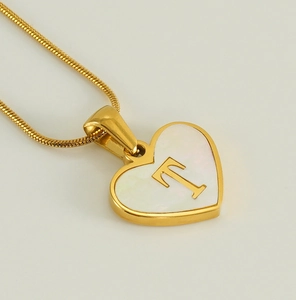 Detail of heart pendant necklace with white shell inlay and gold letter T engraving