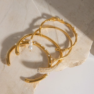 Golden stainless steel pearl bangle set with rhinestones on natural stone background