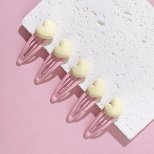 Close-up of five pink metal hair clips with yellow 3D hearts on a textured white block