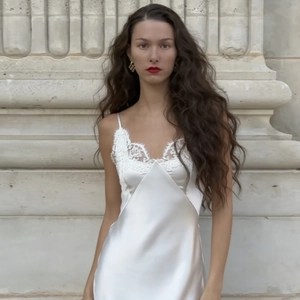 Elegante vestido maxi de satén blanco con encaje en el escote junto a columnas de piedra