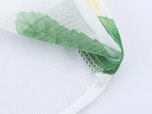 Détail du tissu en mousseline blanche avec feuilles vertes et coutures de précision