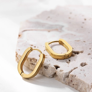 Macro detail of polished 18K gold plated oval hoop earrings on natural stone surface