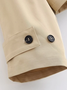 Detail of khaki trench coat sleeve featuring twill fabric and black resin button