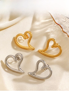 Detail of hollow heart-shaped stud earrings in gold and silver finish on silk background