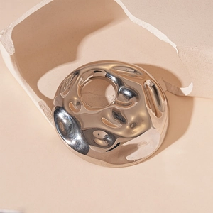 Macro detail of round wrinkled metallic brooch with silver mirror finish and wavy texture