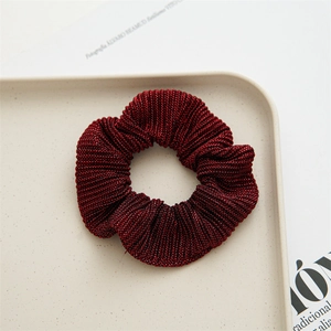 Detailed view of dark red scrunchie made of shiny fabric placed on a beige tray