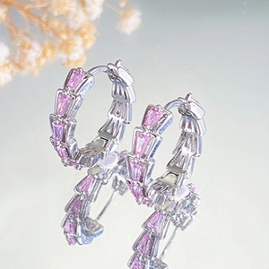 Detail view of silver snake-scale hoop earrings with pink faceted gemstones on a mirror