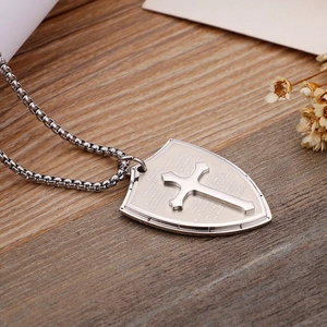 Close-up of silver shield pendant with engraved scripture and cross on metal chain