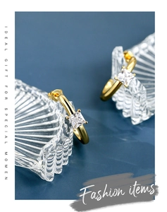 Detailed view of gold C-shaped earrings with square zircon on dark background