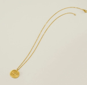 Macro detail of gold coin pendant featuring sunburst engraving and a tiny zircon stone