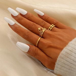 Detailed view of elegant gold crown and textured ring set on hand with white nails