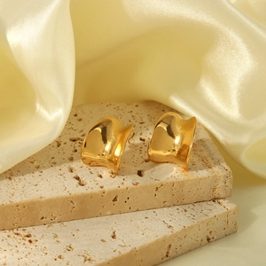 Détail de boucles d'oreilles dorées ondulées sur travertin beige et tissu en soie