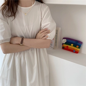 Close-up of a white cotton dress styled with a colorful rainbow knit shoulder bag